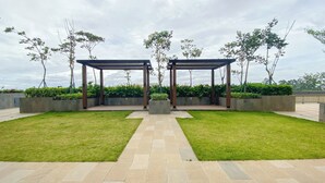 A covered outdoor area with two wooden pergolas, surrounded by well-maintained grass and low hedges.