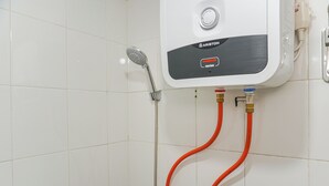 A wall-mounted water heater with a control knob and two red pipes. - Strategic And Warm Studio At Bassura City Apartment (Jakarta)