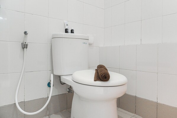 Un inodoro blanco con una toalla sobre la tapa, un accesorio para bidé y un dispensador de papel higiénico.
