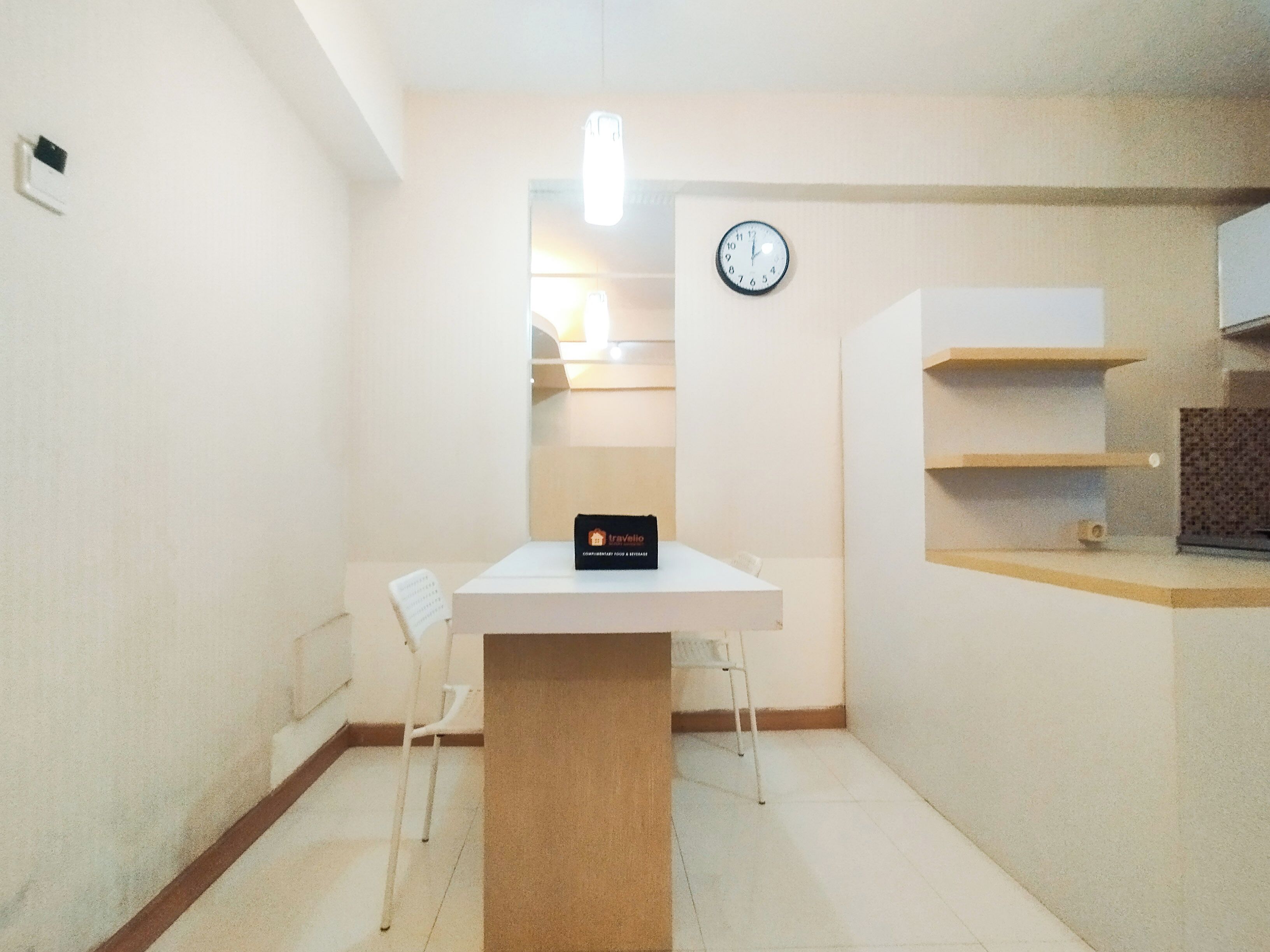 Una habitación pequeña y luminosa con una mesa blanca, un reloj en la pared y un letrero que dice 'Travelio'.