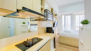 A modern kitchen with a built-in stove, a microwave, and a HAFELLE range hood. There is a bed with a white mattress and a small bedside table. - Cozy Designed Studio Tokyo Riverside Pik 2 Apartment (Jakarta)