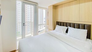 A hotel room with a large bed, a wooden headboard, and a sliding glass door leading to a balcony with a city view. - Cozy Designed Studio Tokyo Riverside Pik 2 Apartment (Jakarta)