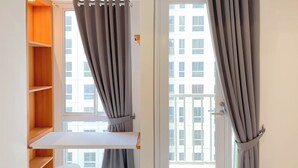 A room with a white desk, grey curtains, and a view of a building through a window. - Pleasurable And Tidy Studio At Tokyo Riverside Pik 2 Apartment (Teluknaga)