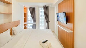 A hotel room with a bed, a TV on the wall, a window with curtains, and a view of buildings outside. - Pleasurable And Tidy Studio At Tokyo Riverside Pik 2 Apartment (Teluknaga)