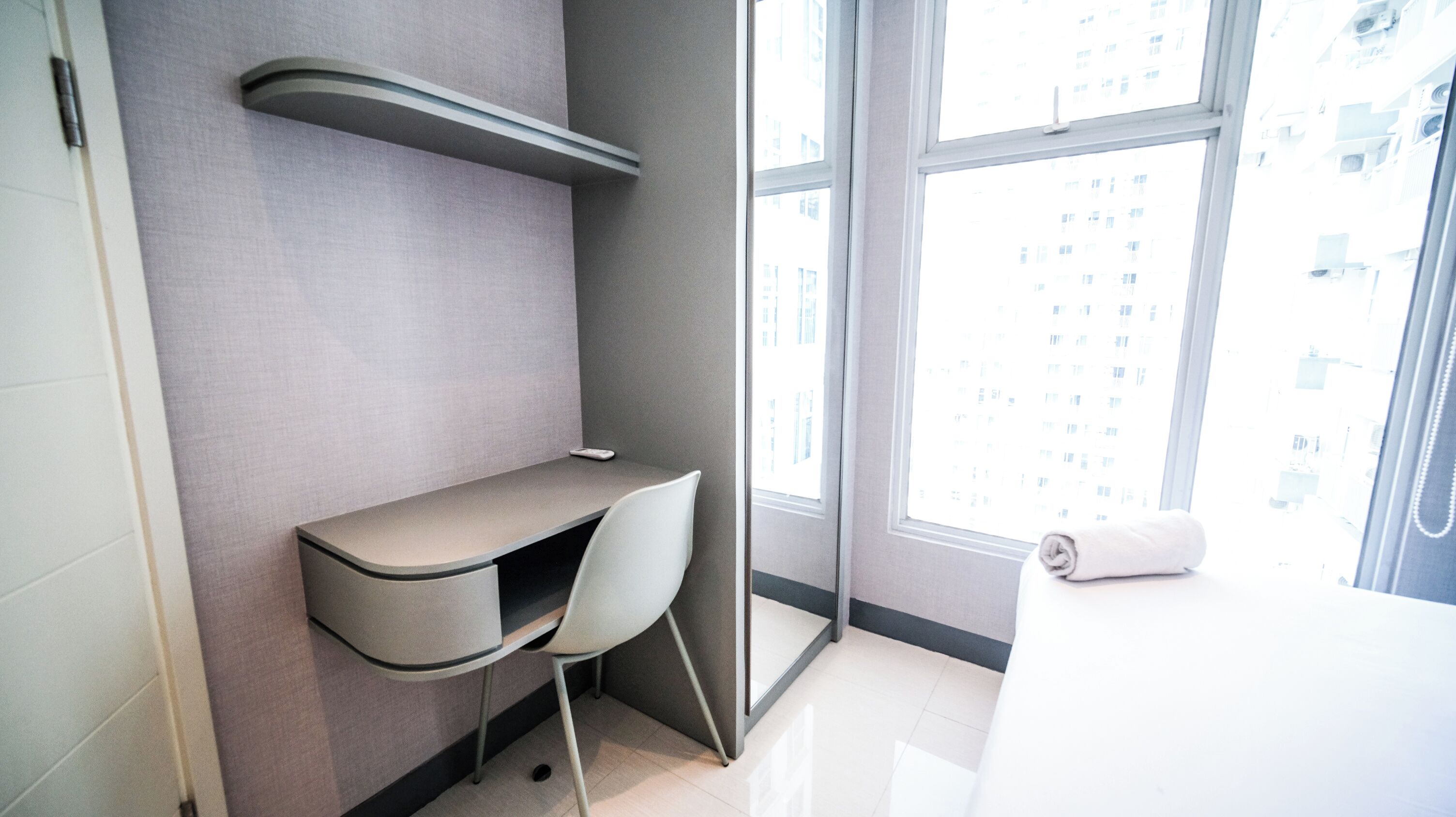 A modern bathroom with a built-in desk, a chair, a towel, and a large window with a city view.