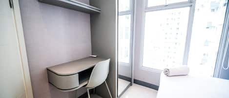 A modern bathroom with a built-in desk, a chair, a towel, and a large window with a city view.