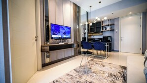 A modern living room with a flat-screen TV, a dining area with two chairs, and a kitchen area with a microwave and coffee maker.