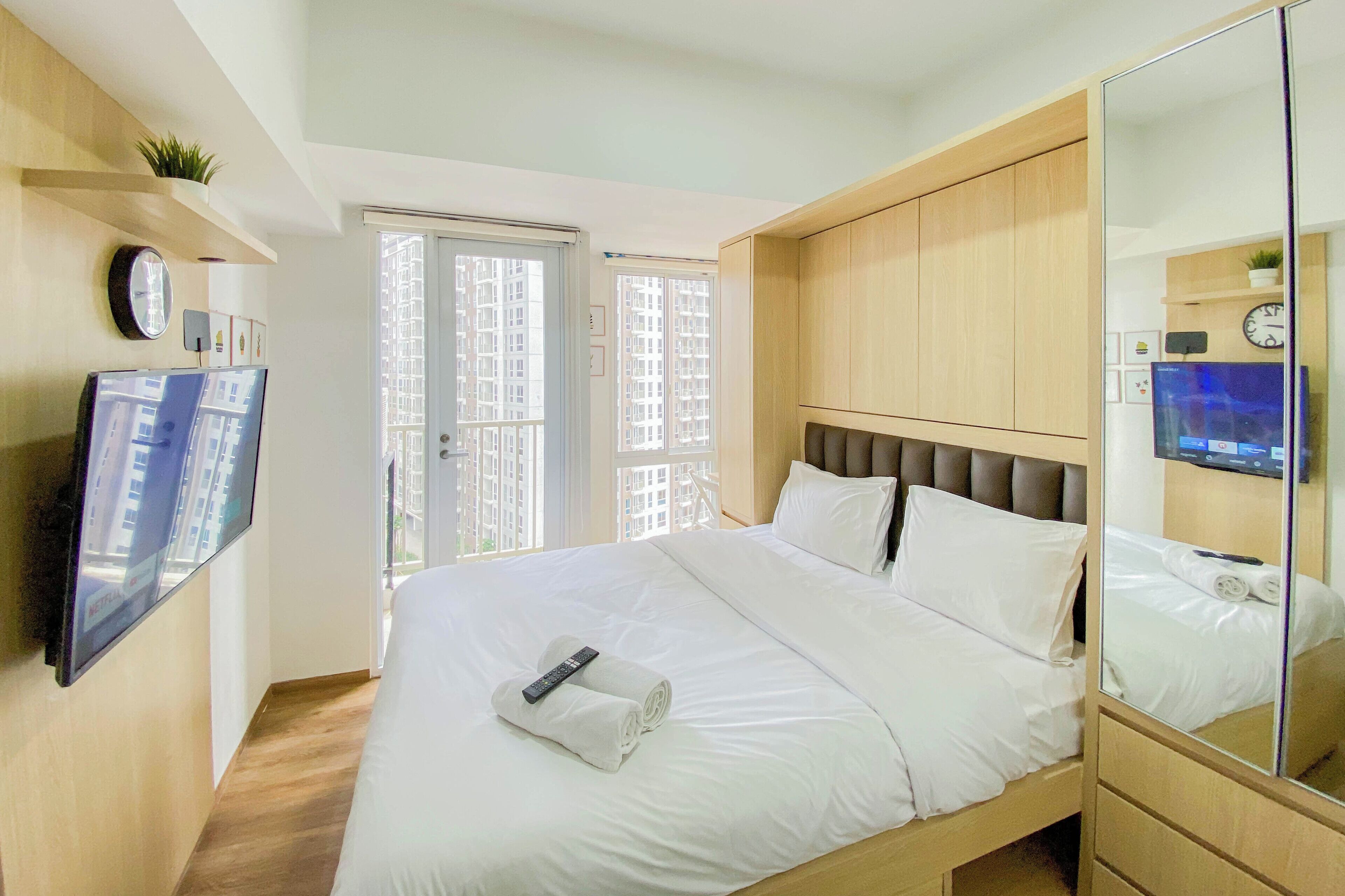 A hotel room with a large bed, a TV mounted on the wall, a mirror, and a sliding door to the balcony.