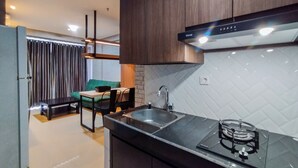 A modern kitchen with a gas stove, a sink, and wooden cabinets. There is a dining area with a green sofa and a table.