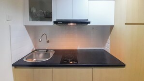 Una cocina con gabinetes blancos, encimera negra, pileta de acero inoxidable y campana extractora integrada.