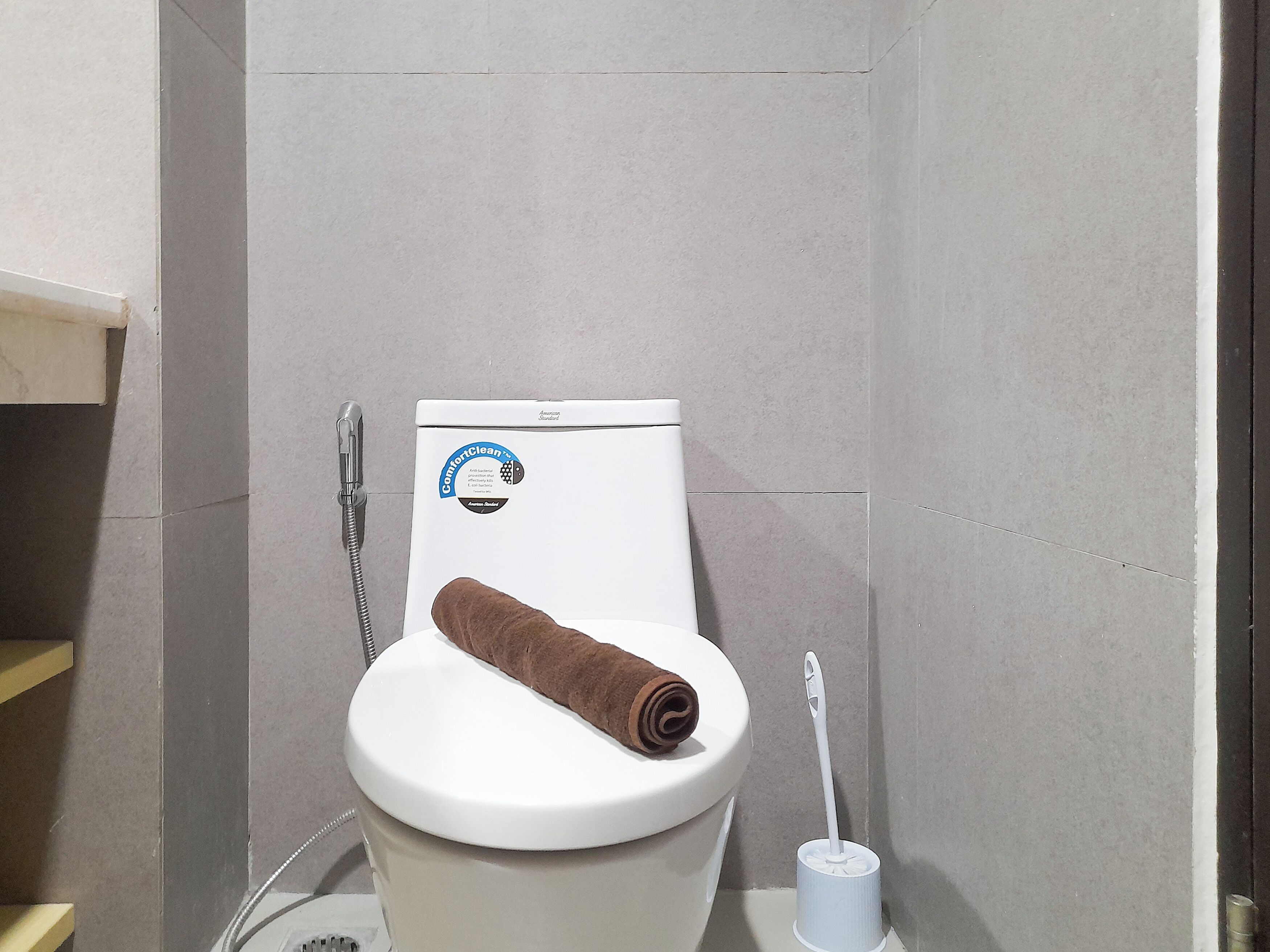 Un inodoro blanco con una toalla marrón sobre el asiento, un escobillón blanco y un cabezal de ducha.
