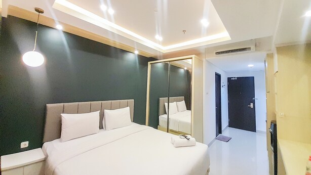 Una habitación de hotel moderna con una cama grande, una mesita de noche, un espejo y una puerta que da a otra estancia.