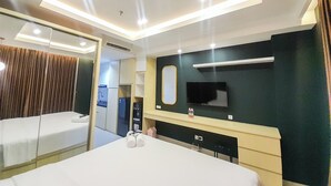Habitación de hotel con cama, escritorio, espejo, televisor y baño visible a través de una puerta abierta.