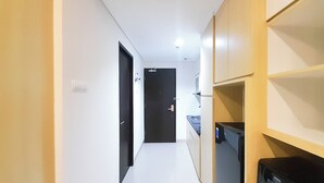 Un pasillo estrecho con una puerta negra al final, paredes blancas y un armario de madera con un electrodoméstico negro a la derecha.