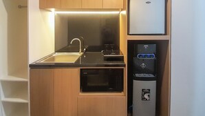 A compact kitchen with a sink, microwave, and a water dispenser. - Tranquil And Modern Studio At Mataram City Apartment (Ngaglik)