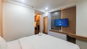 A hotel room with a bed, a television mounted on the wall, and a wooden panel design. - Tranquil And Modern Studio At Mataram City Apartment (Ngaglik)