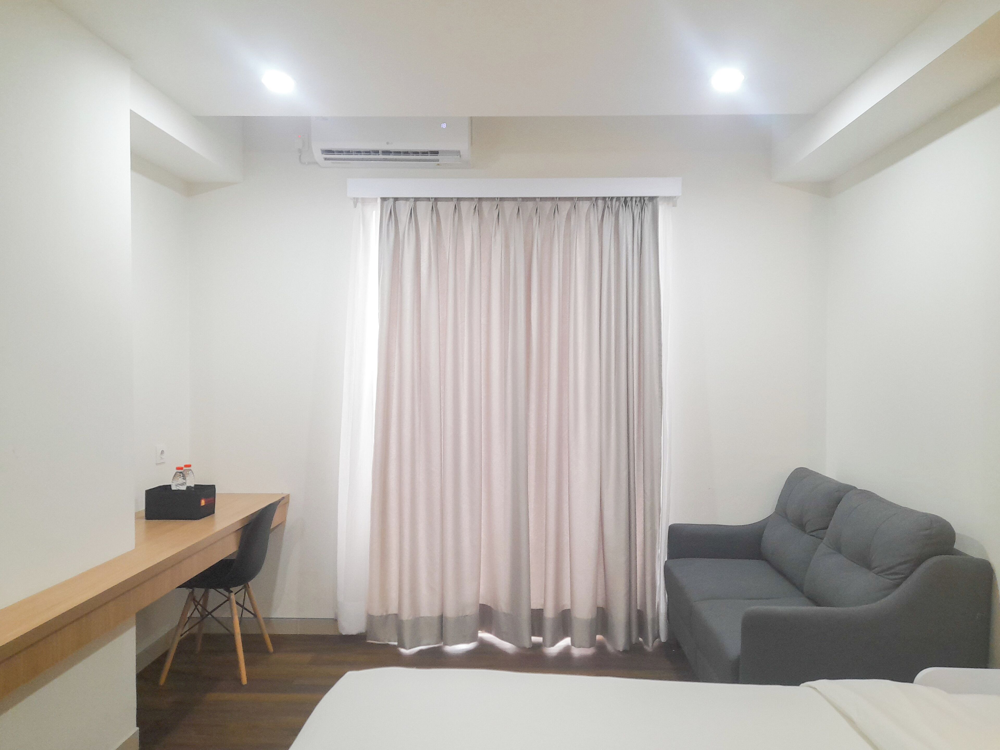 A hotel room with a bed, a desk with a chair, a grey sofa, and a window with curtains.