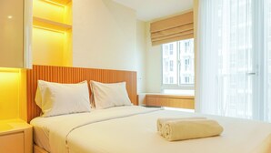 A hotel room with a large bed, bedside tables, a window with curtains, and a view of buildings outside. - Comfortable Design Studio At Tokyo Riverside Pik 2 Apartment (Teluknaga)