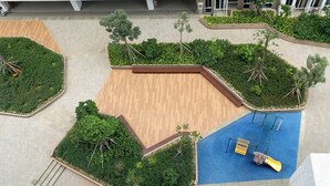 An aerial view of a landscaped outdoor area with a wooden deck, a blue play area with a slide, and various green plants and trees. - Comfortable Design Studio At Tokyo Riverside Pik 2 Apartment (Teluknaga)