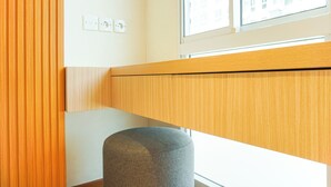 A modern room with a wooden headboard, a grey ottoman, and a window with a view of buildings. - Comfortable Design Studio At Tokyo Riverside Pik 2 Apartment (Teluknaga)