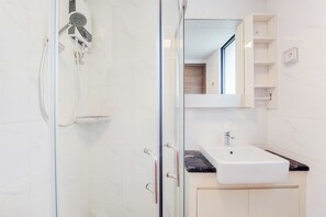 Un baño moderno con cabina de ducha de vidrio, un lavabo blanco y un espejo sobre él.