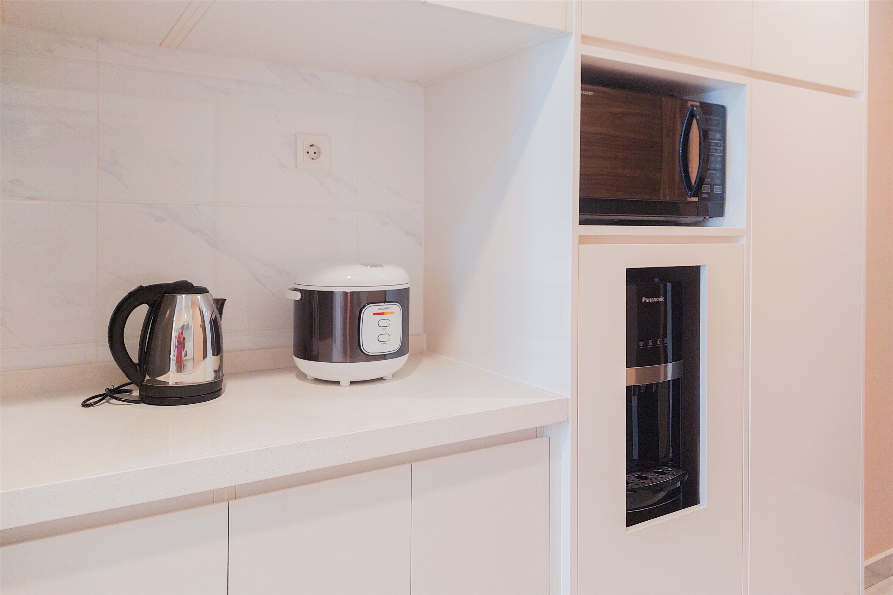A kitchen with a kettle, a rice cooker, and a coffee machine on a white countertop.