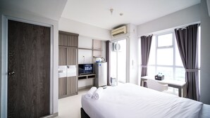 A hotel room with a bed, a desk with a computer, a wardrobe, and a bathroom with a shower. - Best Studio At Taman Melati Surabaya Apartment (Surabaya)