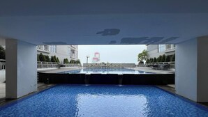 An indoor swimming pool with clear water, surrounded by a white building with balconies. - Best Studio At Taman Melati Surabaya Apartment (Surabaya)