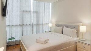 Ein Hotelzimmer mit einem großen Bett, zwei Nachttischen, einem an der Wand befestigten Fernseher und einem Fenster mit Vorhängen.