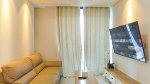 Ein modernes Wohnzimmer mit Sofa, Couchtisch, flachbildfernseher an der Wand und einem Fenster mit Vorhängen.