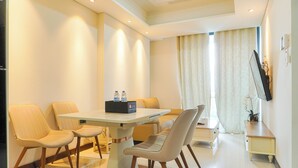 Ein modernes Hotelzimmer mit Essbereich, inklusive Tisch und vier Stühlen, einem wandmontierten Flachbildfernseher sowie einem kleinen Beistelltisch mit Vase und Pflanze.