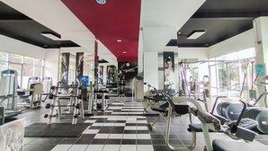 Ein Fitnessraum mit unterschiedlichen Trainingsgeräten, einem Schachbrettmuster-Boden und großen Fenstern für natürliches Licht.