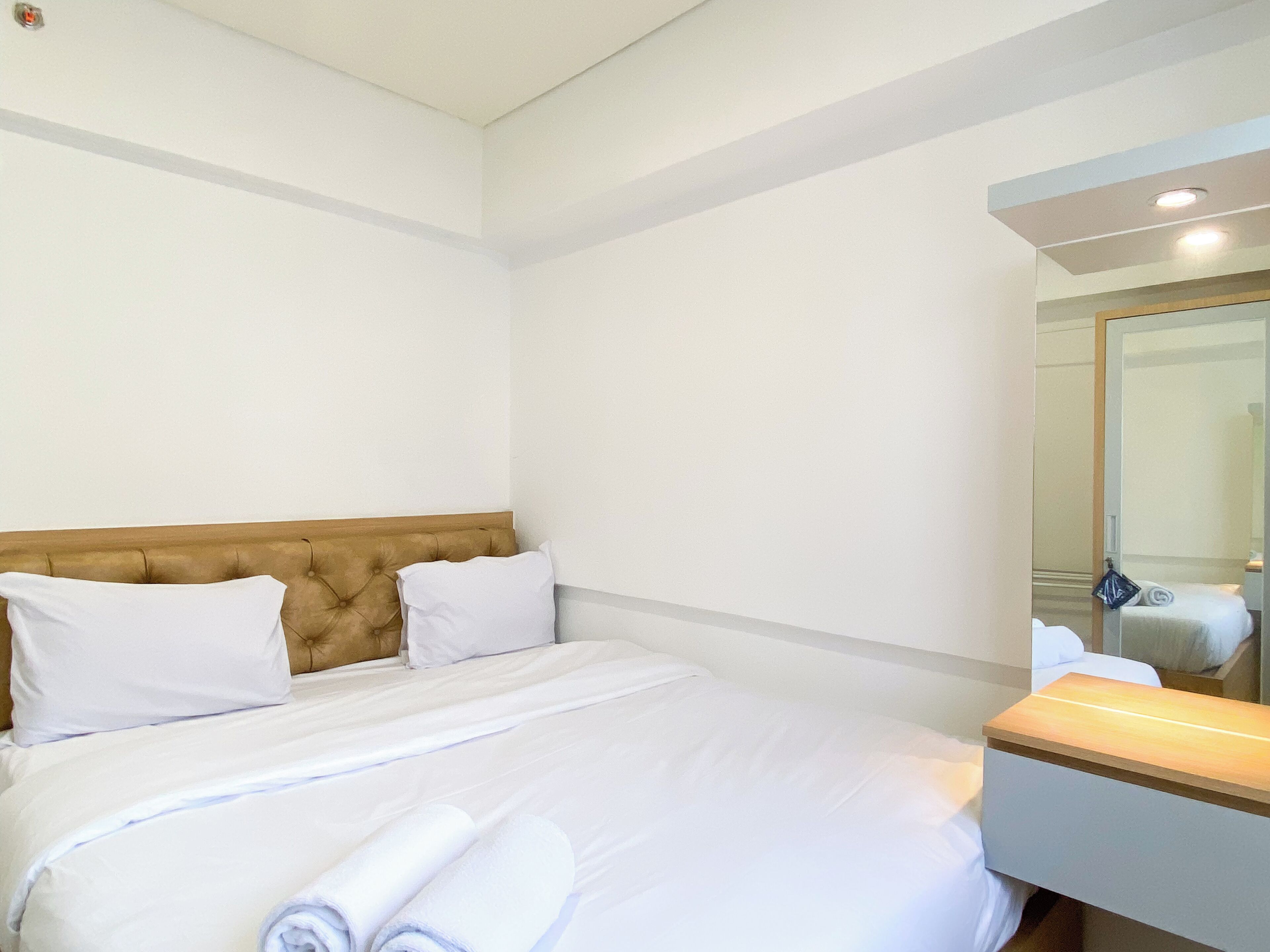 A hotel room with a bed, a wooden headboard, white bedding, a bedside table, and a mirror.