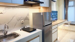 A modern kitchen with a built-in induction cooktop, stainless steel refrigerator, and a digital TV display. - Comfort Living Studio Pollux Chadstone Apartment (Cikarang)