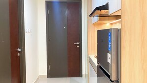 A kitchen with a refrigerator, a wooden cabinet, and a door. - Comfort Living Studio Pollux Chadstone Apartment (Cikarang)