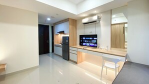 A modern kitchen with a built-in TV, a refrigerator, and a dining area with a chair. - Comfort Living Studio Pollux Chadstone Apartment (Cikarang)