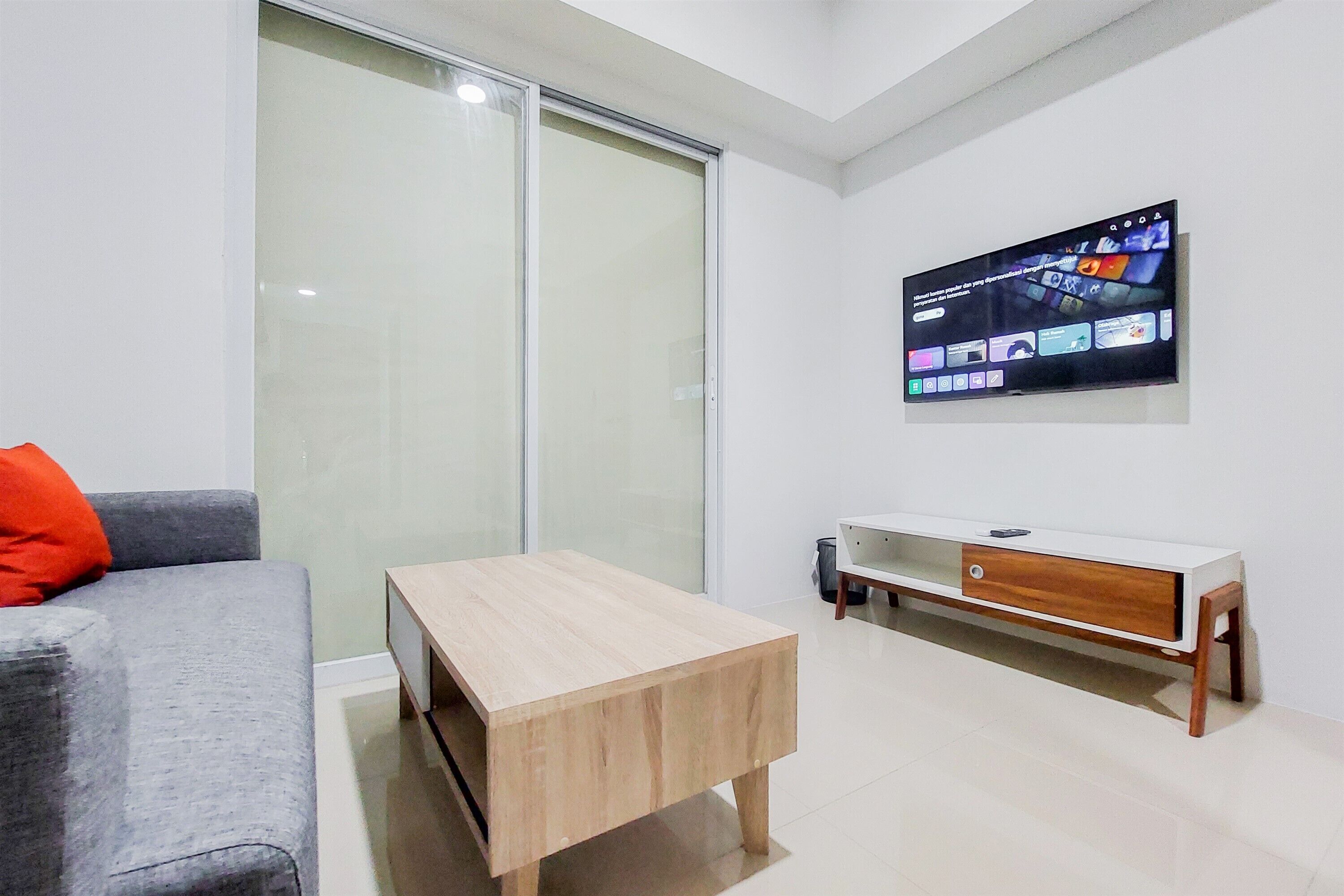 A modern living room with a grey sofa, a wooden coffee table, a white TV stand, and a sliding glass door.