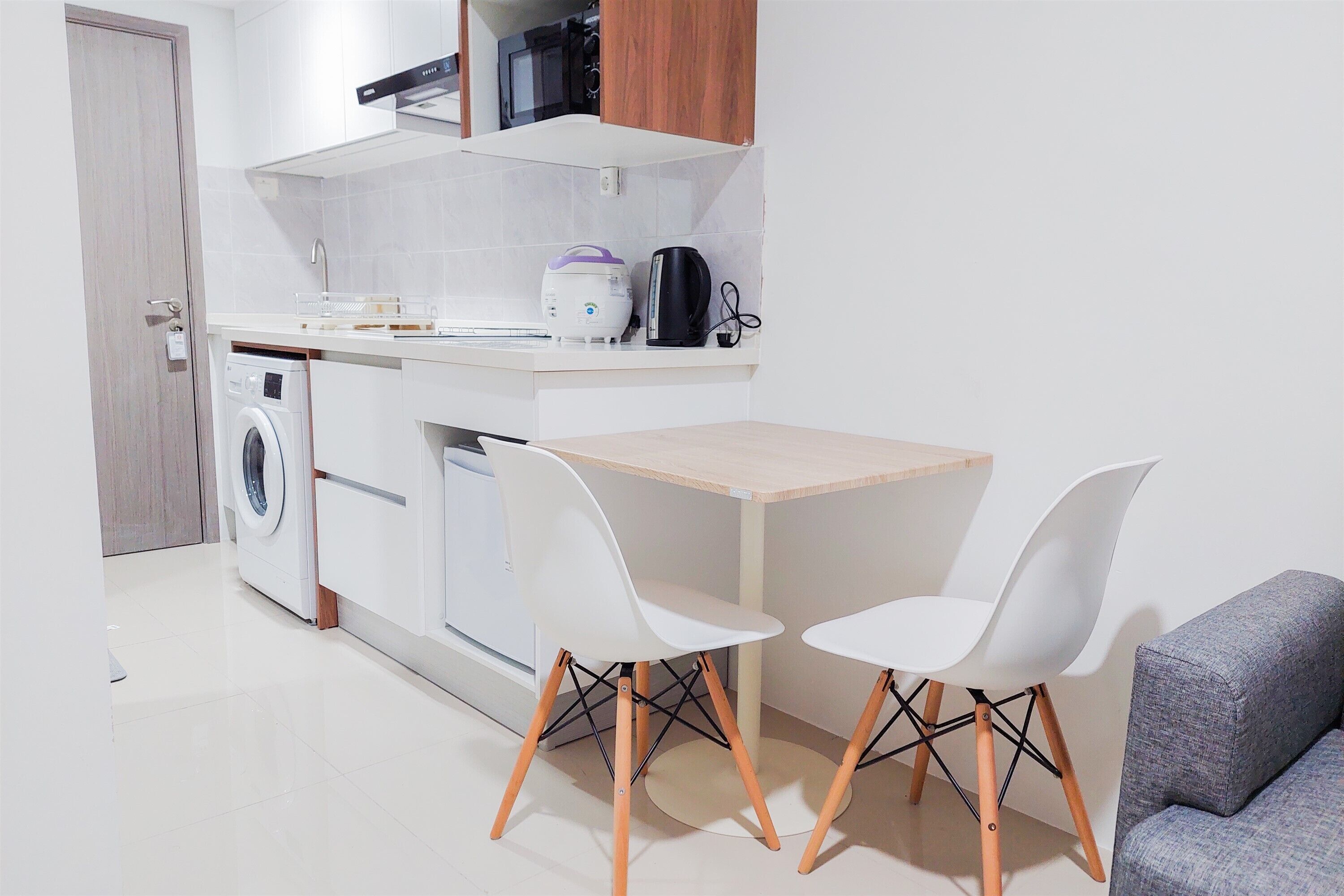 A compact kitchen with a washing machine, a coffee maker, and a microwave. There is a small dining table with two chairs.