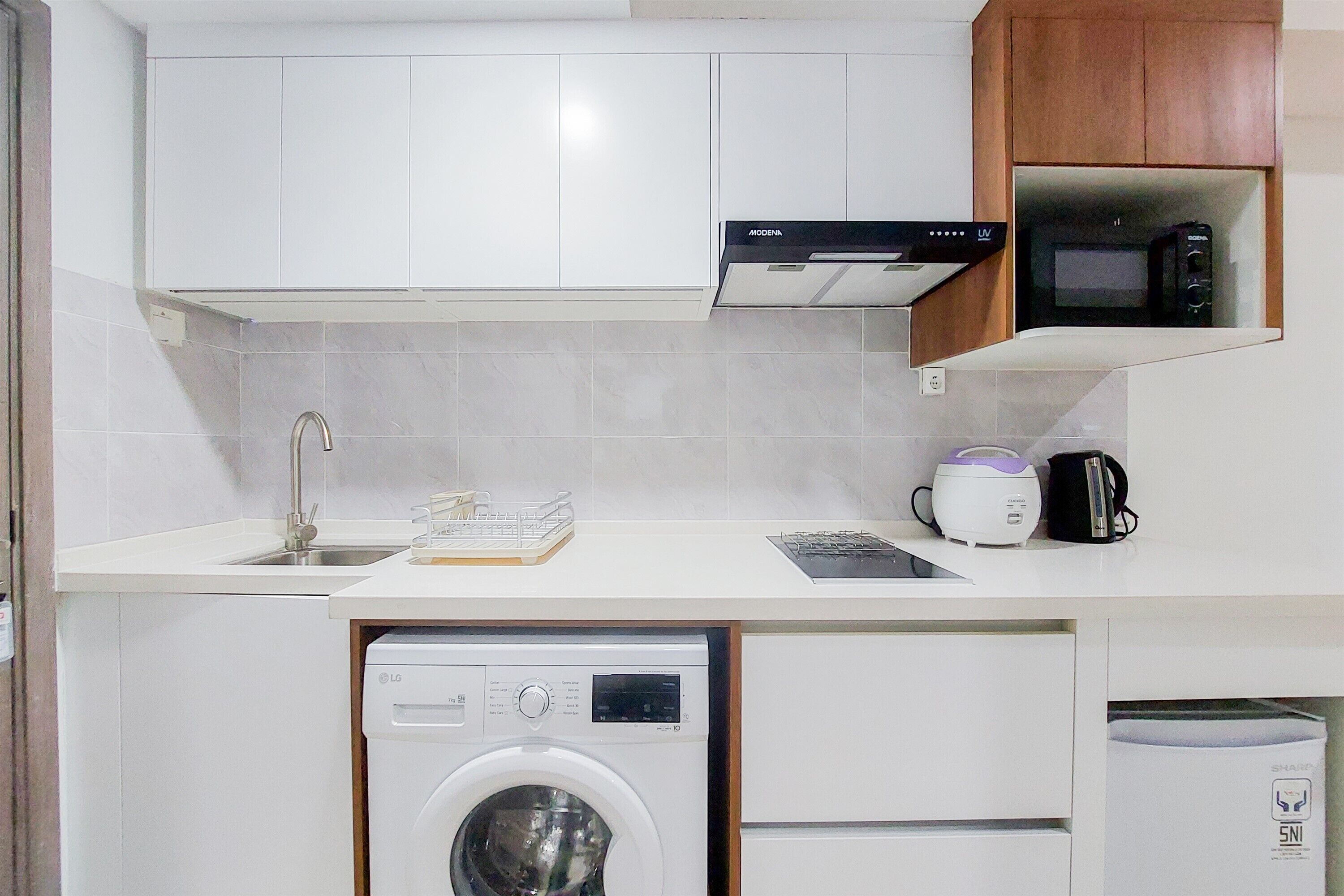 A compact kitchen with white cabinets, a built-in washing machine, a microwave, and a coffee maker.