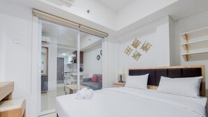 A hotel room with a bed, a desk, a chair, a wardrobe, and a bathroom visible through a glass door. - Minimalist 1Br At Tamansari Bintaro Mansion Apartment (South Tangerang)