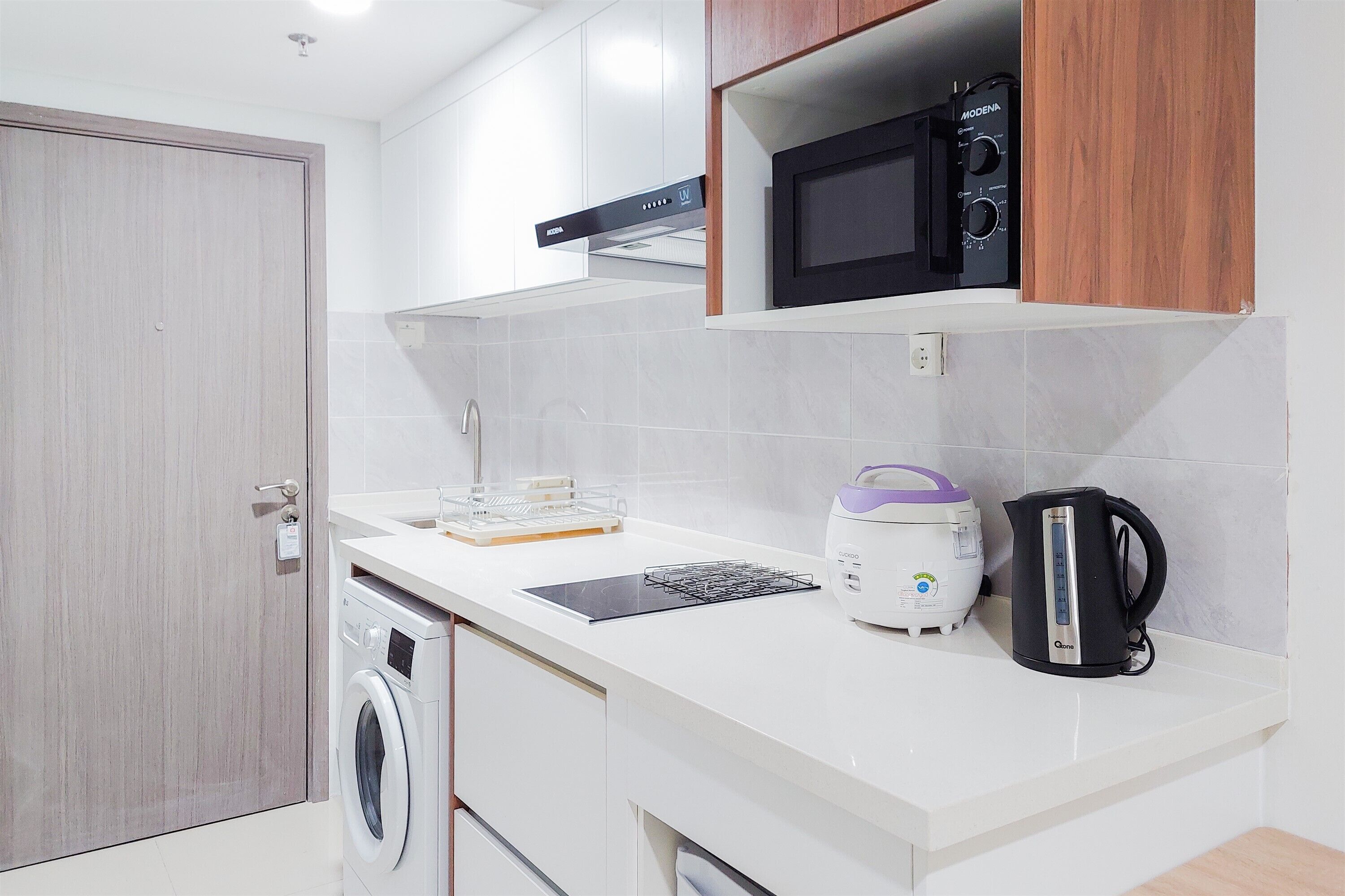Cocina compacta con lavadora, microondas y hervidor sobre la encimera.
