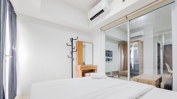 A hotel room with a bed, a wooden nightstand, a mirror, and a sliding glass door leading to a bathroom. - Minimalist 1Br At Tamansari Bintaro Mansion Apartment (South Tangerang)