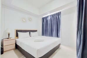 A neatly made bed with white linens, a wooden headboard, and a bedside table with a lamp and phone. - Cozy And Comfort Living 1Br Tamansari Bintaro Mansion Apartment (South Tangerang)