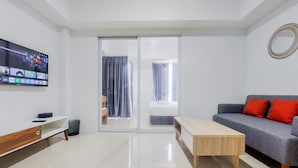 A modern living room with a flat-screen TV, a grey sofa with red cushions, a wooden coffee table, and a sliding glass door leading to a balcony. - Comfort Living And Homey 1Br Tamansari Bintaro Mansion Apartment (South Tangerang)