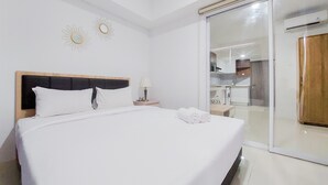 A hotel room with a bed, a nightstand, a lamp, and a sliding glass door leading to a kitchenette. - Comfort Living And Homey 1Br Tamansari Bintaro Mansion Apartment (South Tangerang)