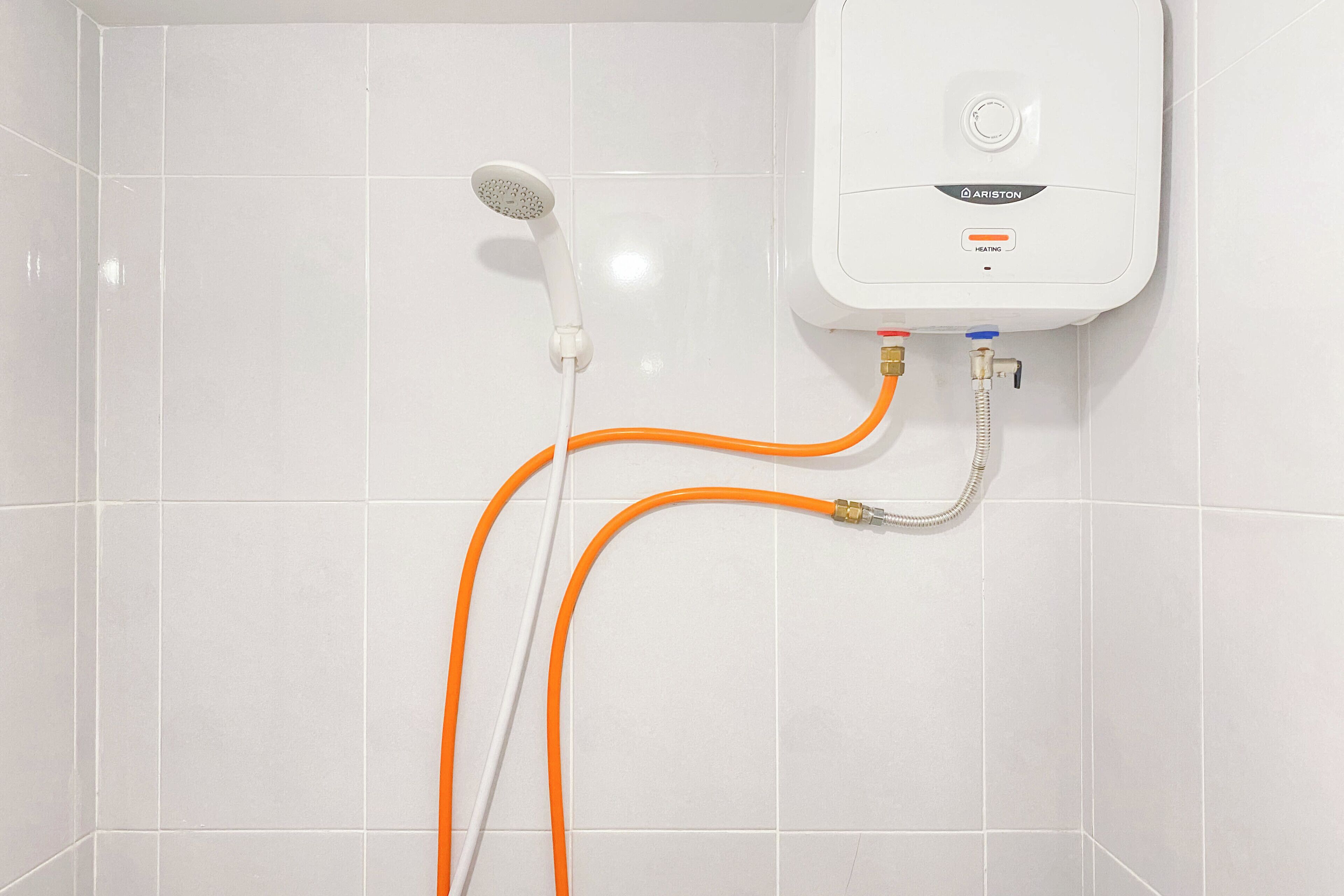 Un área de ducha con azulejos blancos, un cabezal de ducha de mano y un panel de control en la pared.
