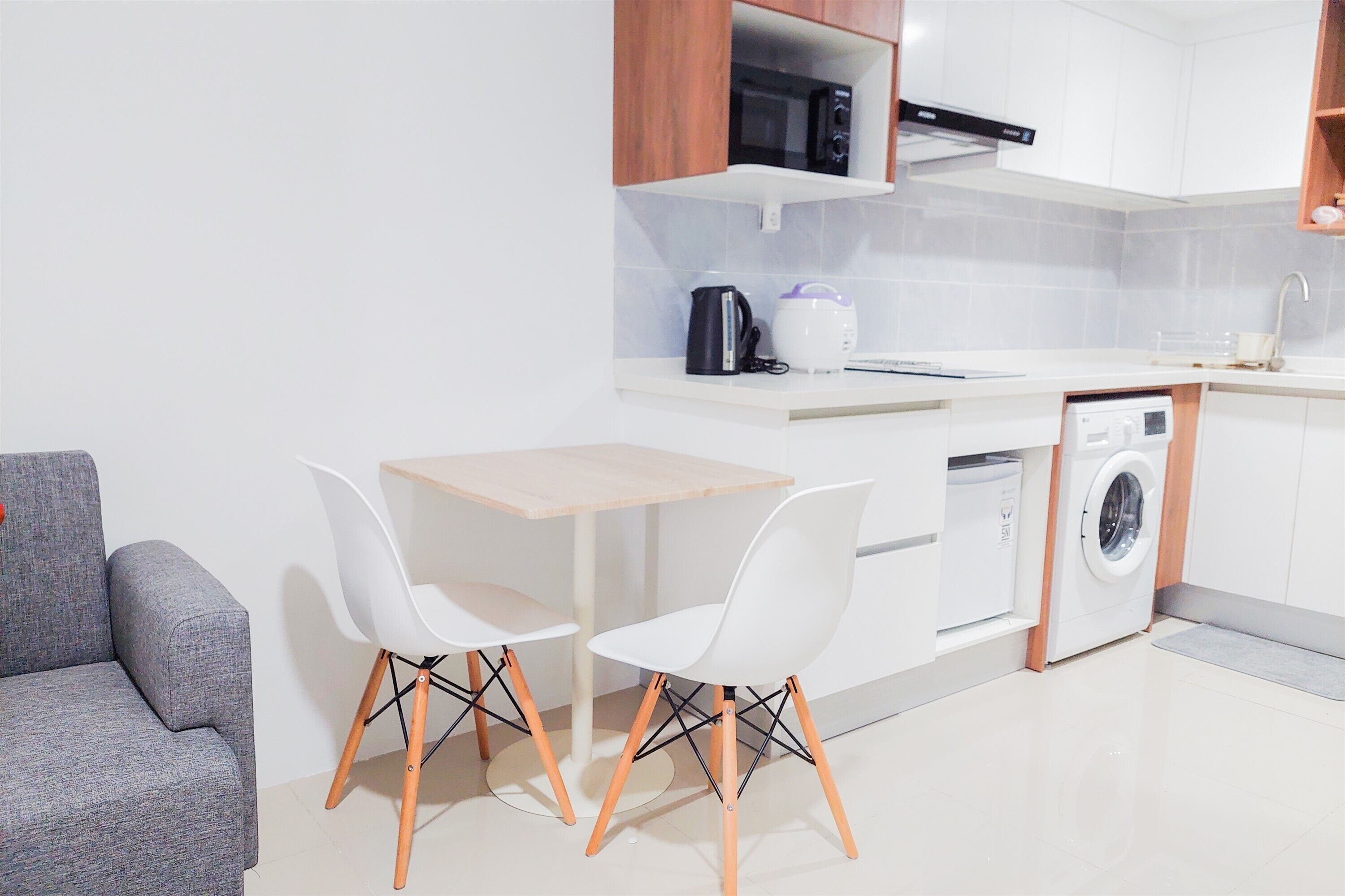 A modern kitchen with white cabinetry, a microwave, a coffee maker, and a dishwasher. There is a small dining table with two white chairs.