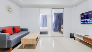 A modern living room with a grey sofa, a wooden coffee table, a TV mounted on the wall, and a sliding glass door leading to a bedroom. - Homey And Cozy Living 1Br Tamansari Bintaro Mansion Apartment (South Tangerang)
