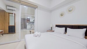A hotel room with a large bed, a sliding glass door leading to a bathroom, and two wall-mounted mirrors. - Homey And Cozy Living 1Br Tamansari Bintaro Mansion Apartment (South Tangerang)