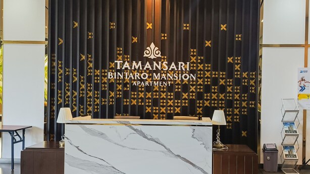 A reception desk with a marble top, a black backdrop with golden patterns, and a logo for Tamansari Bintang Mansion Apartment. - Homey And Cozy Living 1Br Tamansari Bintaro Mansion Apartment (South Tangerang)